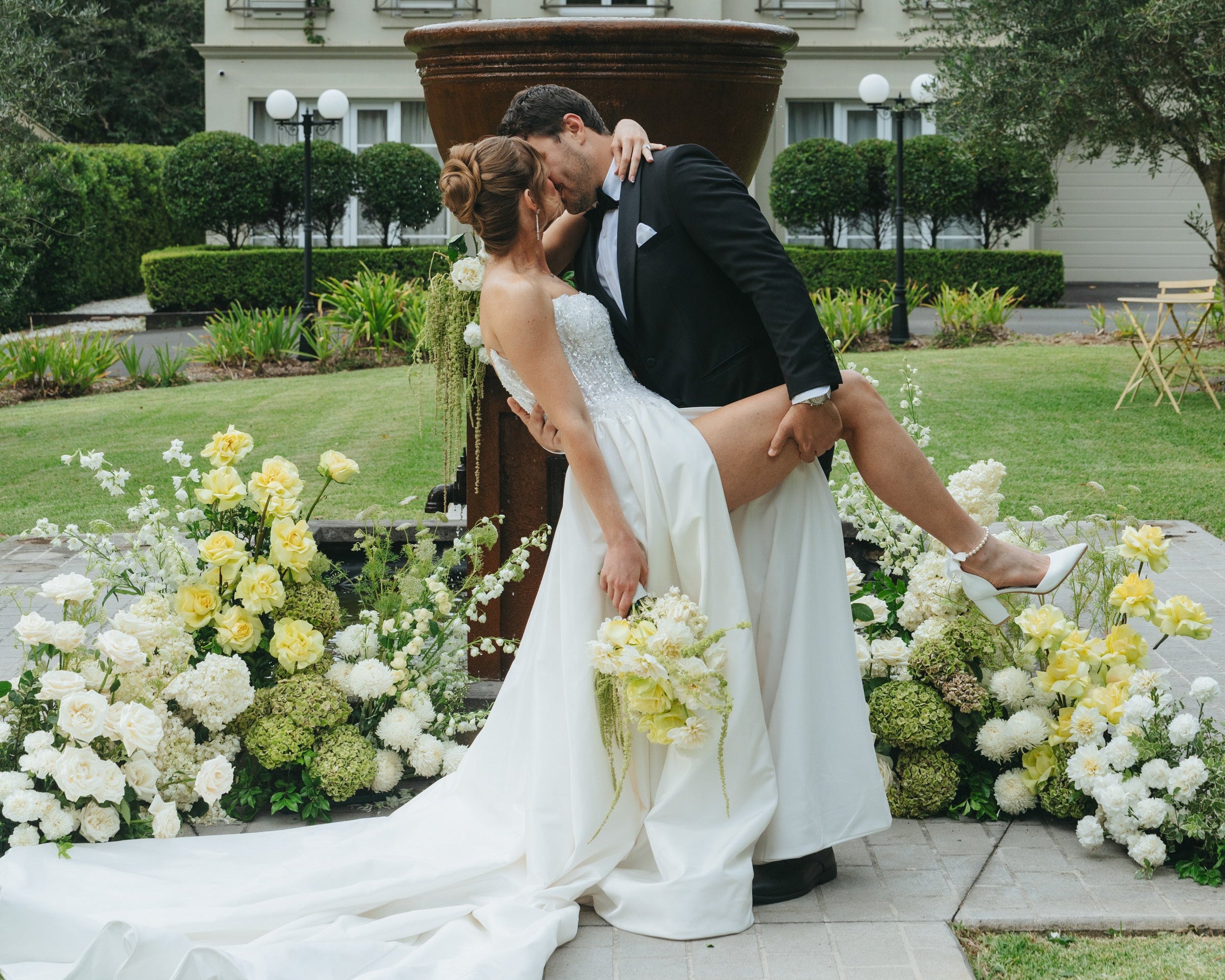 Wedding couple kissing surrounded by floral nest with a house in the background